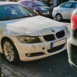 White BMW sedan with front-end damage parked on a busy city street.