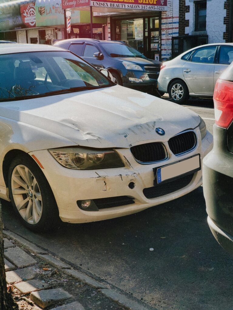 White BMW sedan with front-end damage parked on a busy city street.